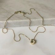 A gold chain necklace with a shell shaped charm.