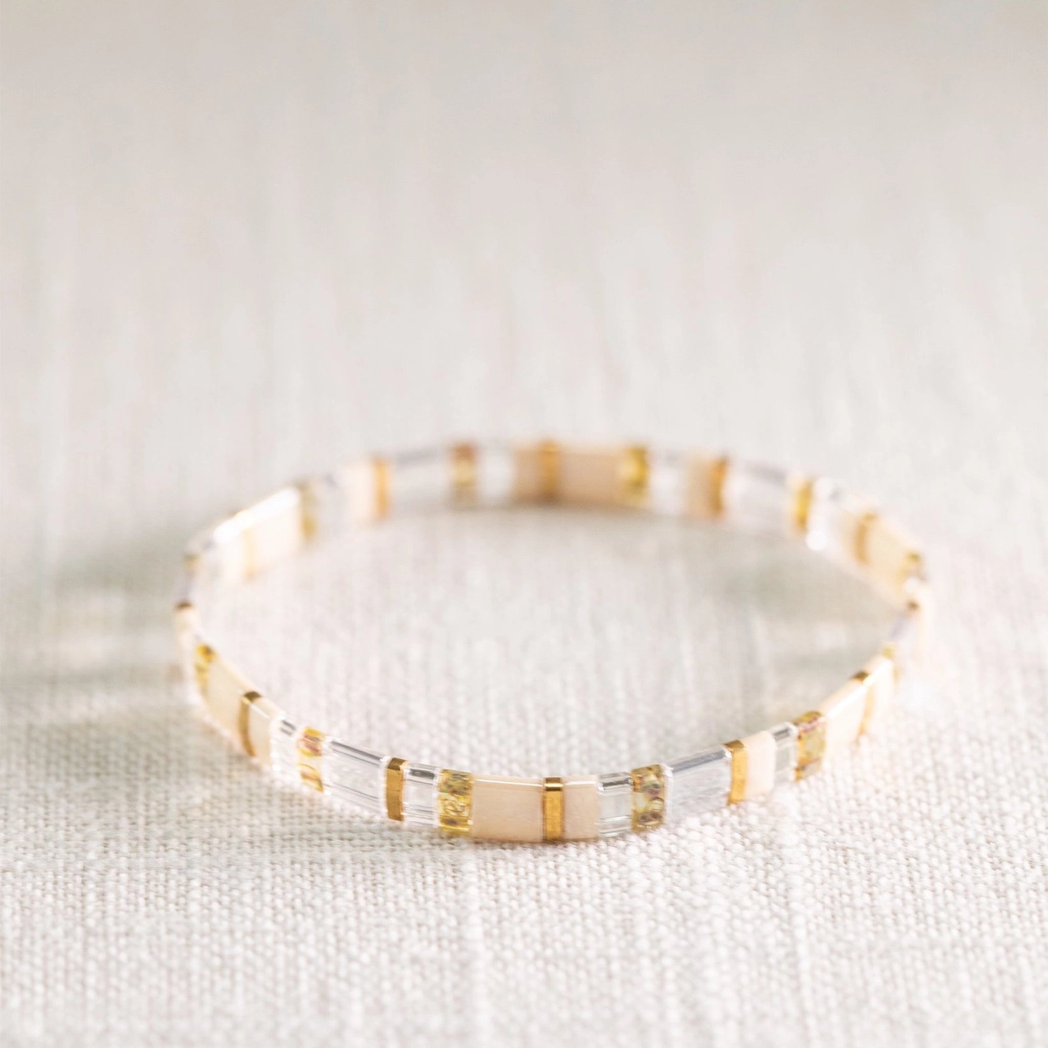 A gold, clear and neutral colored bracelet with a variation of alternating beads. 