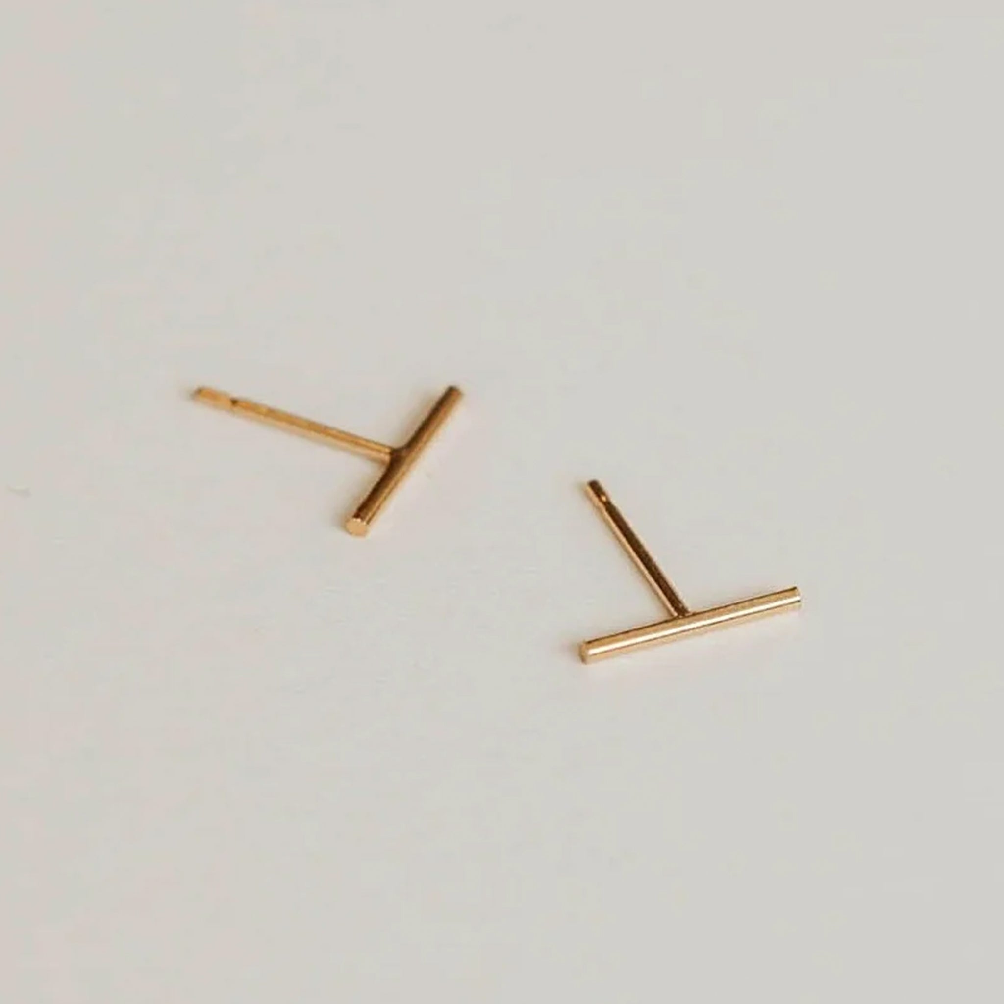 On a grey background is a pair of gold dainty bar stud earring. 