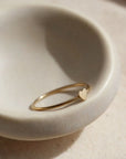 In a neutral ceramic bowl is a dainty gold ring with a tiny heart in the center.