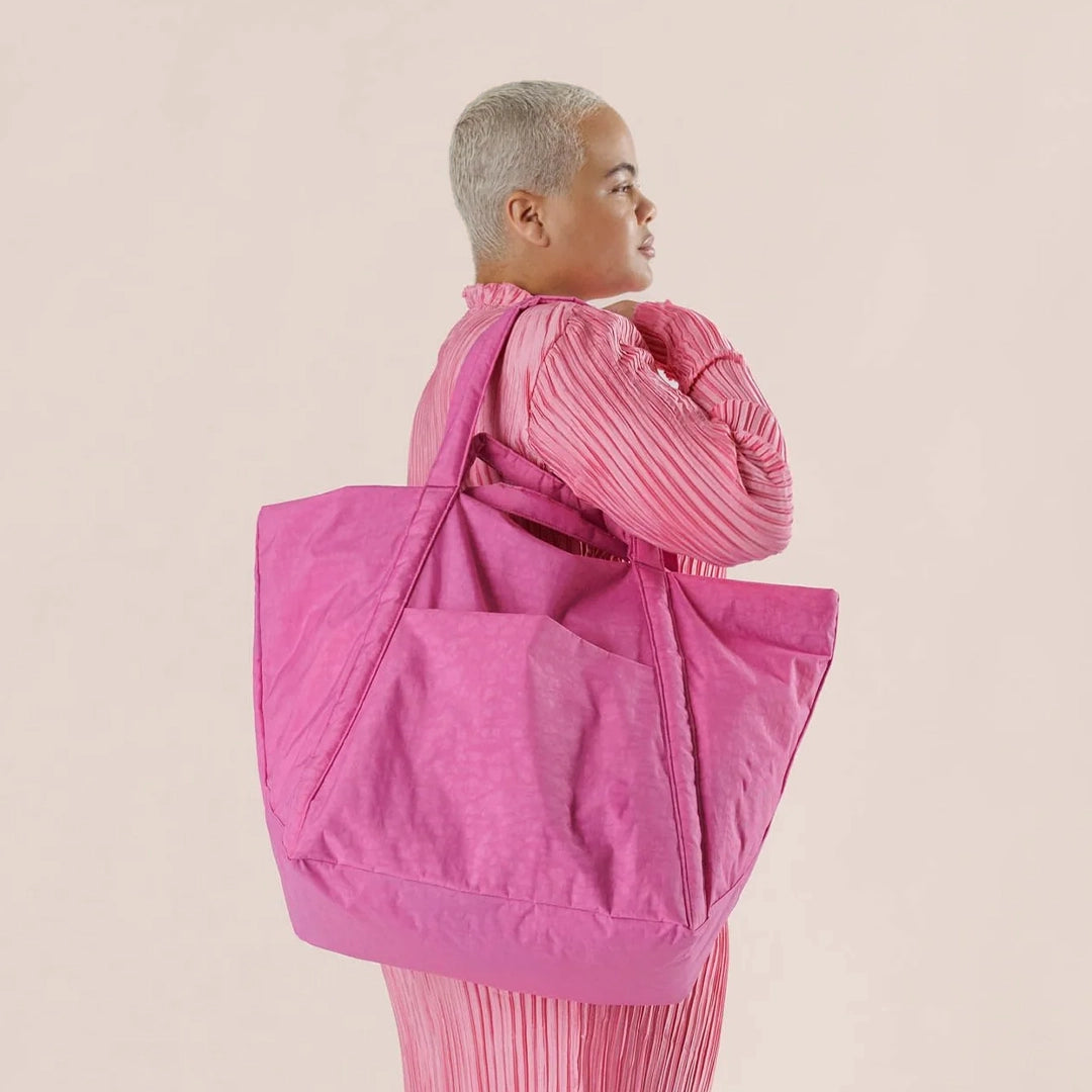 On a cream background is a nylon tote bag in a bright pink shade with two handles and an outside pocket.