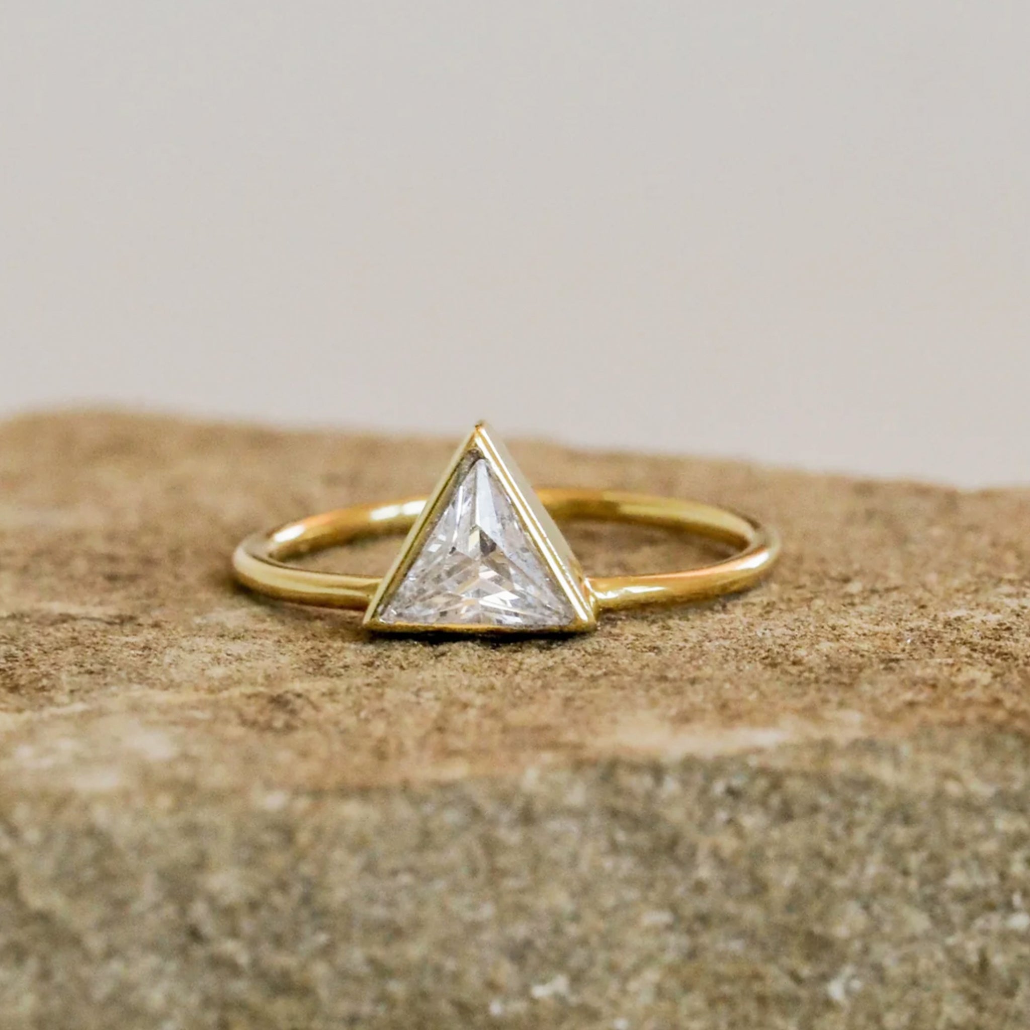 A gold ring with a triangle CZ stone in the center. 