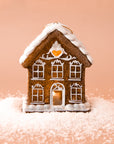 A gingerbread house shaped ornament with white pipping details and lights coming from the inside.