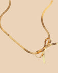 A gold herringbone chain necklace tied in a bow.