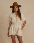 A natural colored short sleeve jumpsuit with a cinched waist and front pockets as well as a stitched rope heart detail on the back.