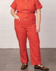 On a white background is a model wearing a short sleeve jumpsuit with a collar, side pockets and a gold zipper going down the front.