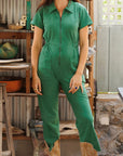 A model wearing a green short sleeve jumpsuit with a zipper going up the front, a collar and front pockets.