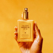 A bottle of shimmer body oil with gold flecks and a pump applicator.