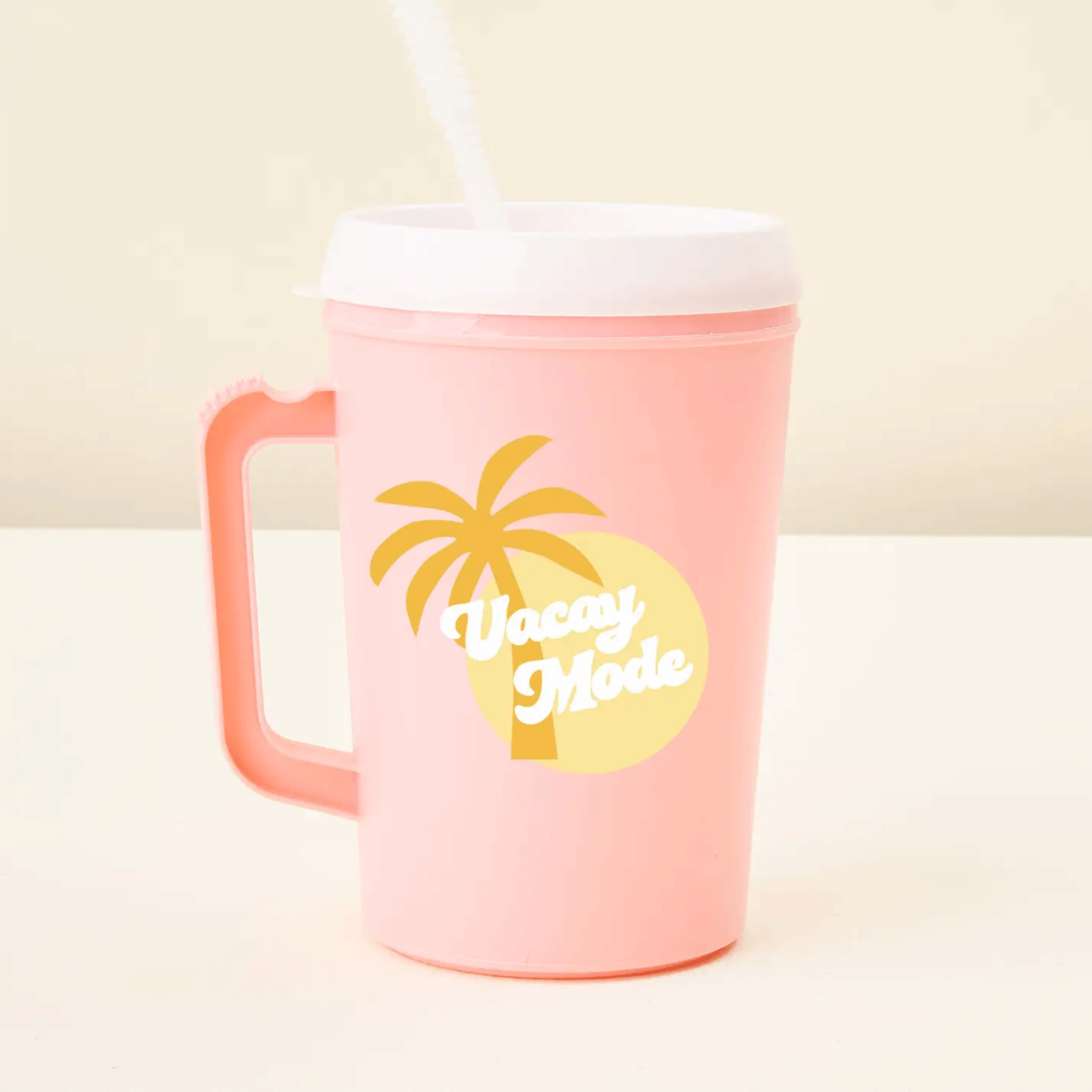 On a tan background is a pink travel mug with a handle and a white lid and plastic straw along with a yellow sun and palm graphic and text that reads, &quot;Vacay Mode&quot;. 