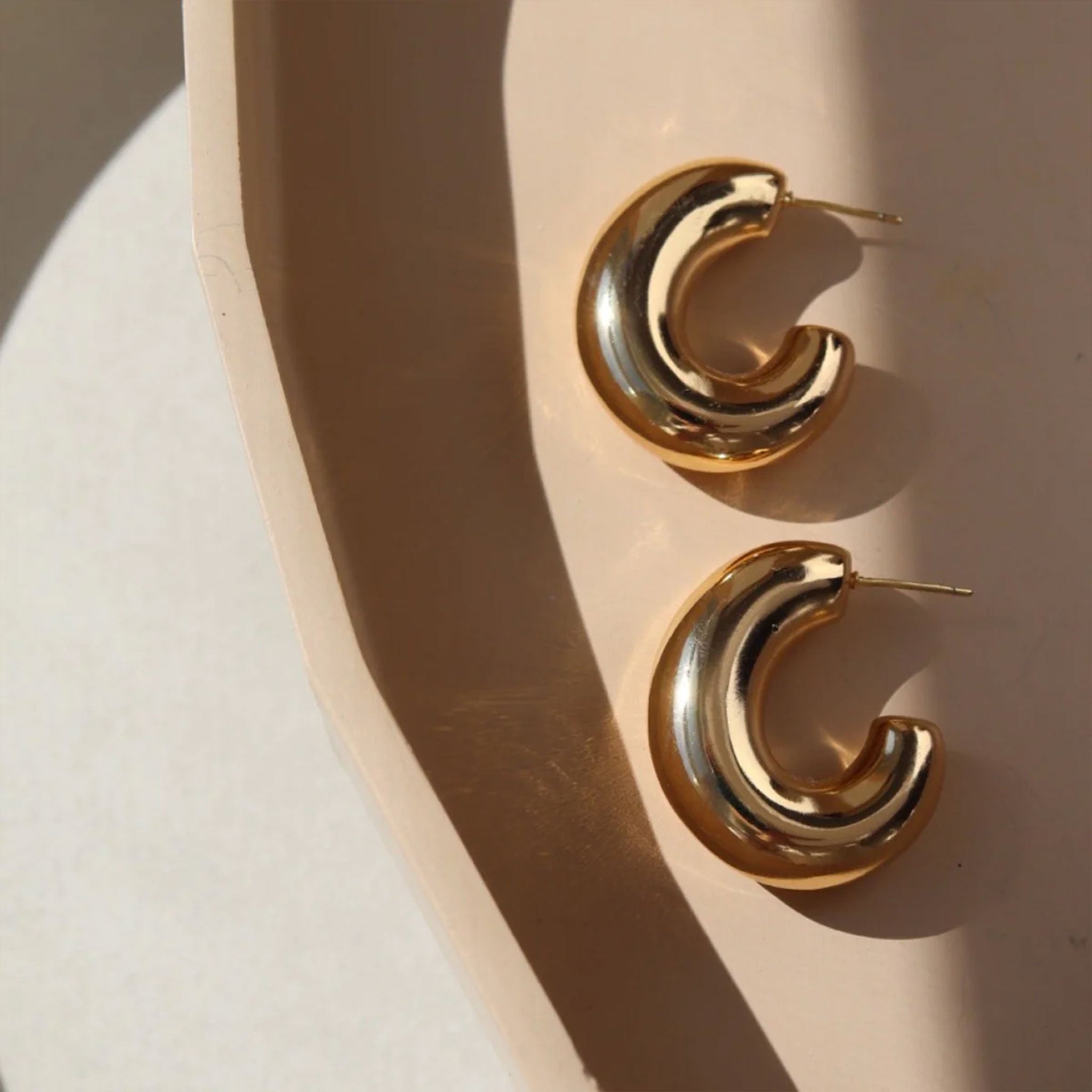 A pair of chunky gold hoops laying on a neutral plate. 