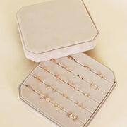 A cream velvet square jewelry box with slots for earrings and rings.