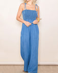 A mid blue shade of denim in a smocked jumpsuit with tie shoulder straps.