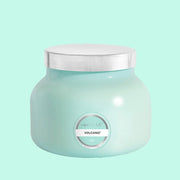 On a blue background is an aqua blue glass jar candle with a silver lid on top