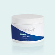 A plastic white jar sits in front of a light peach background. On the body of the jar there is a sticker wrap that is split diagonally by color. The top half is white and the bottom half is cobalt blue. On the blue side there is a small, turquoise rectangle with white text. Under the turquoise rectangle there is white text that reads ‘Volcano body cream.’