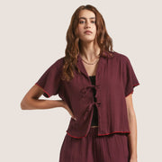 A short sleeved port wine colored top with red piping and front tie details.