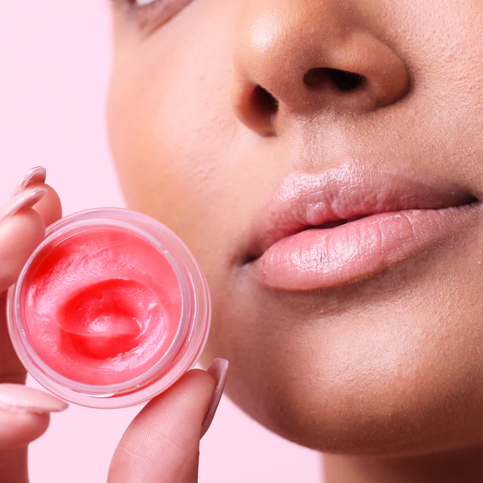 A model holding the small jar of pink lip balm. 