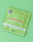 On a green background is a green packet with a single feminine wipe inside. The packaging reads, "sweetums taste below the waist".