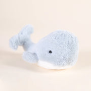 A light blue/gray whale stuffed animal with a fuzzy texture and a split tail and black friendly beaded eyes.