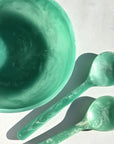 A teal green set of a wavy resin salad bowl and two serving utensils.