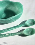 A teal green set of a wavy resin salad bowl and two serving utensils.