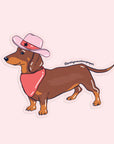 On a pink background is a weenie dog sticker with a bandana and pink cowboy hat on.
