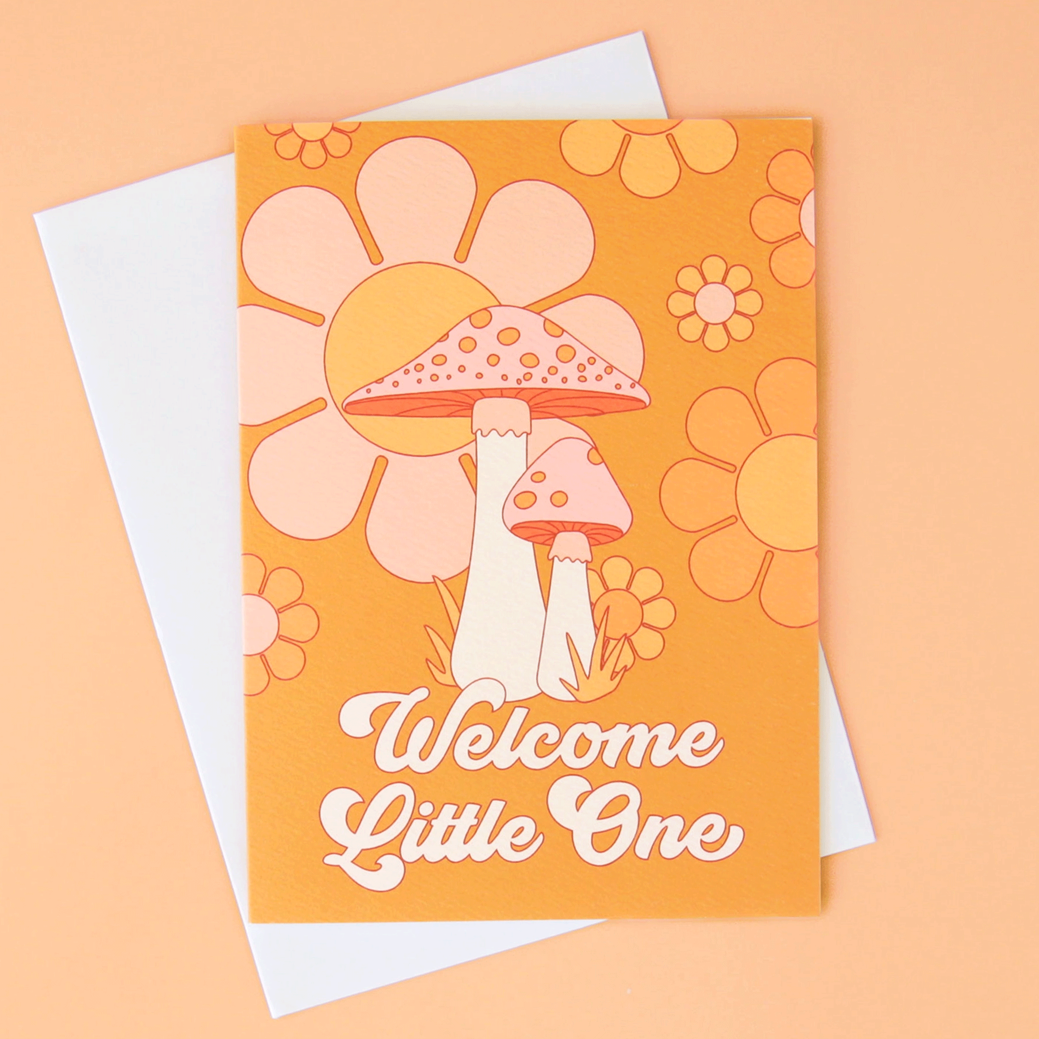 On a peachy background is an orange card with a floral and mushroom design along with white text that reads, "Welcome Little One".