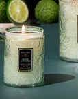 A green glass decorative candle with a single wick and black rectangle label in front that reads, "Voluspa White Cypress".