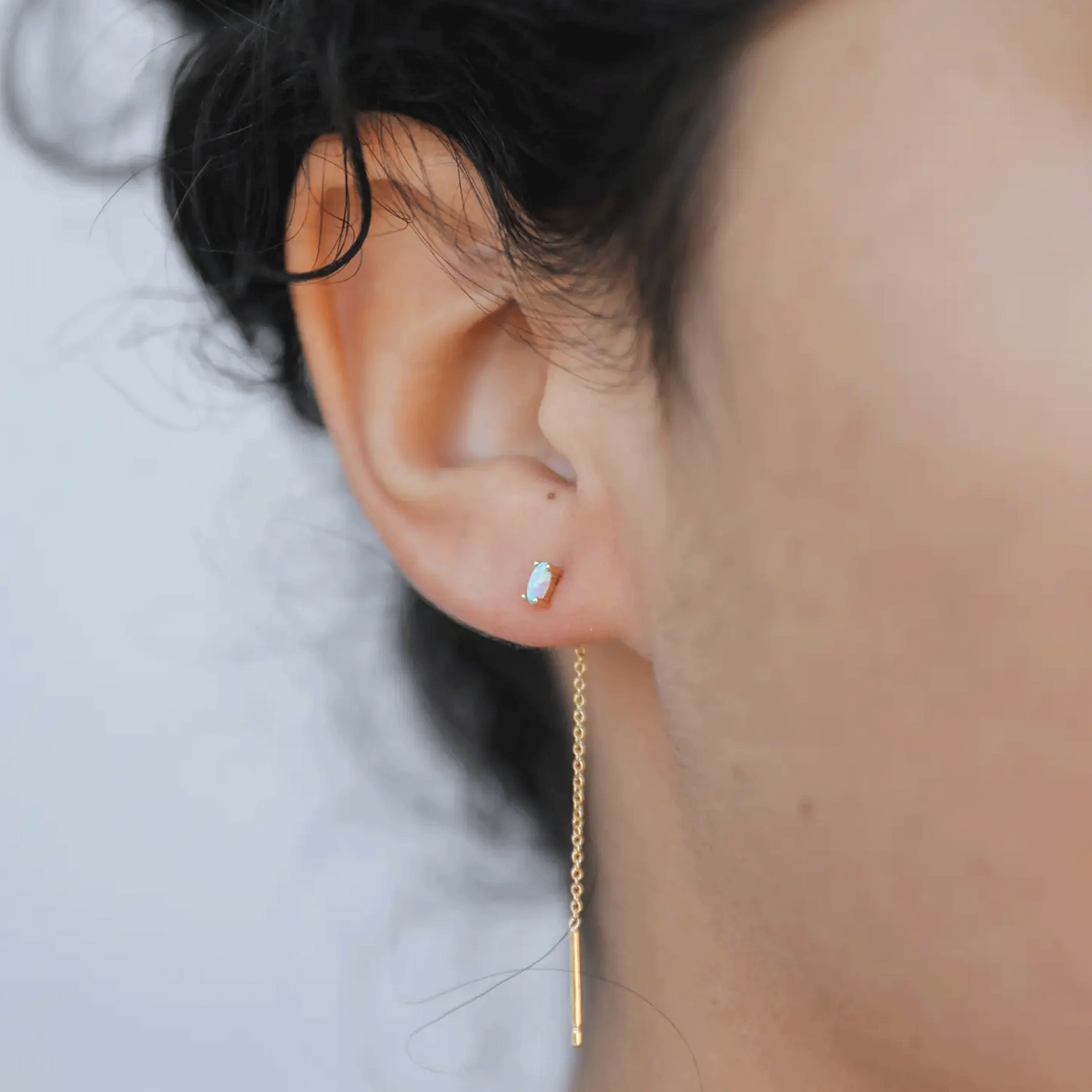 A model wearing a white opal stud with a gold chain thread in the back dangling down. 