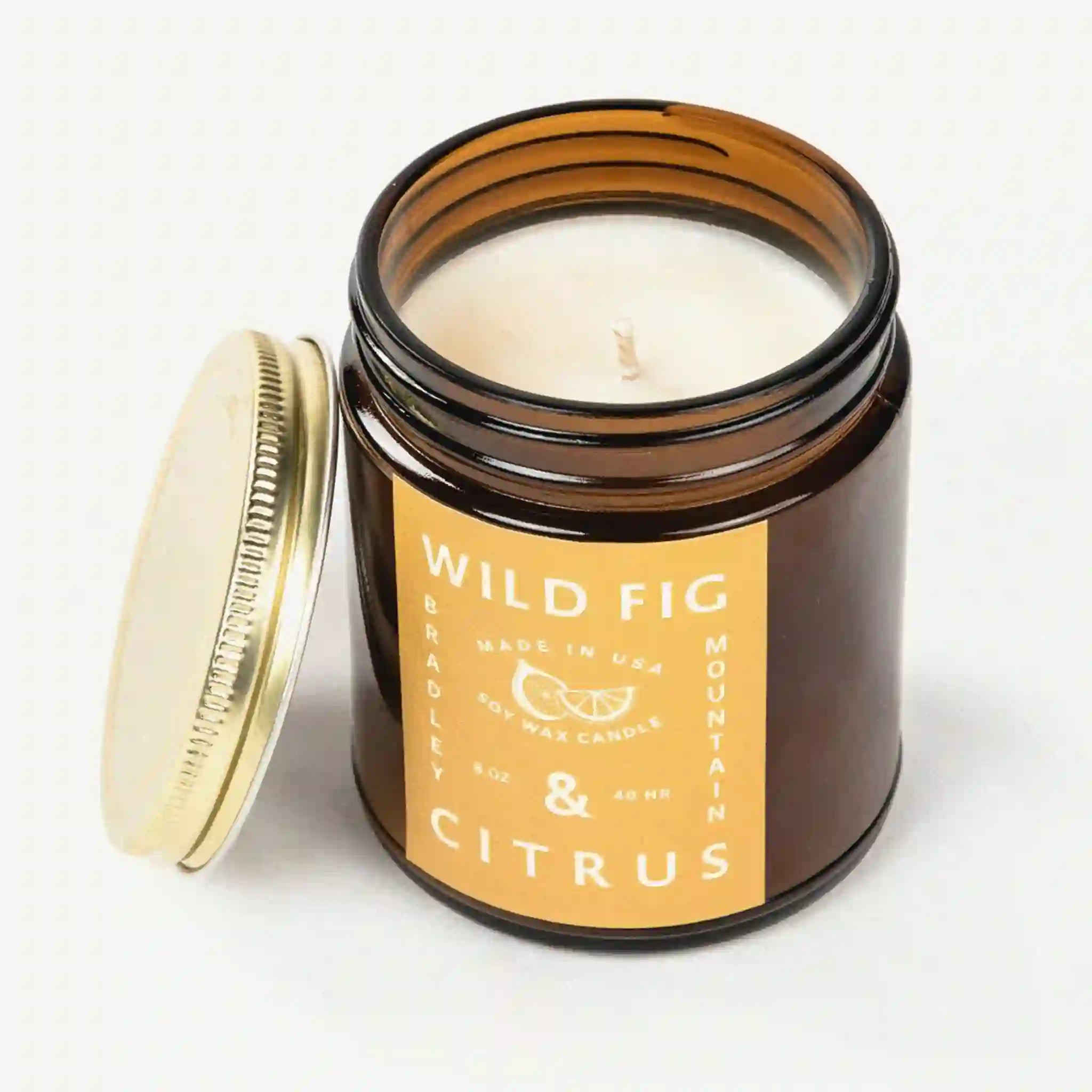 On a white background is an amber colored jar candle with a yellow label and white text that reads, &quot;Wild Fig &amp; Citrus&quot;. 