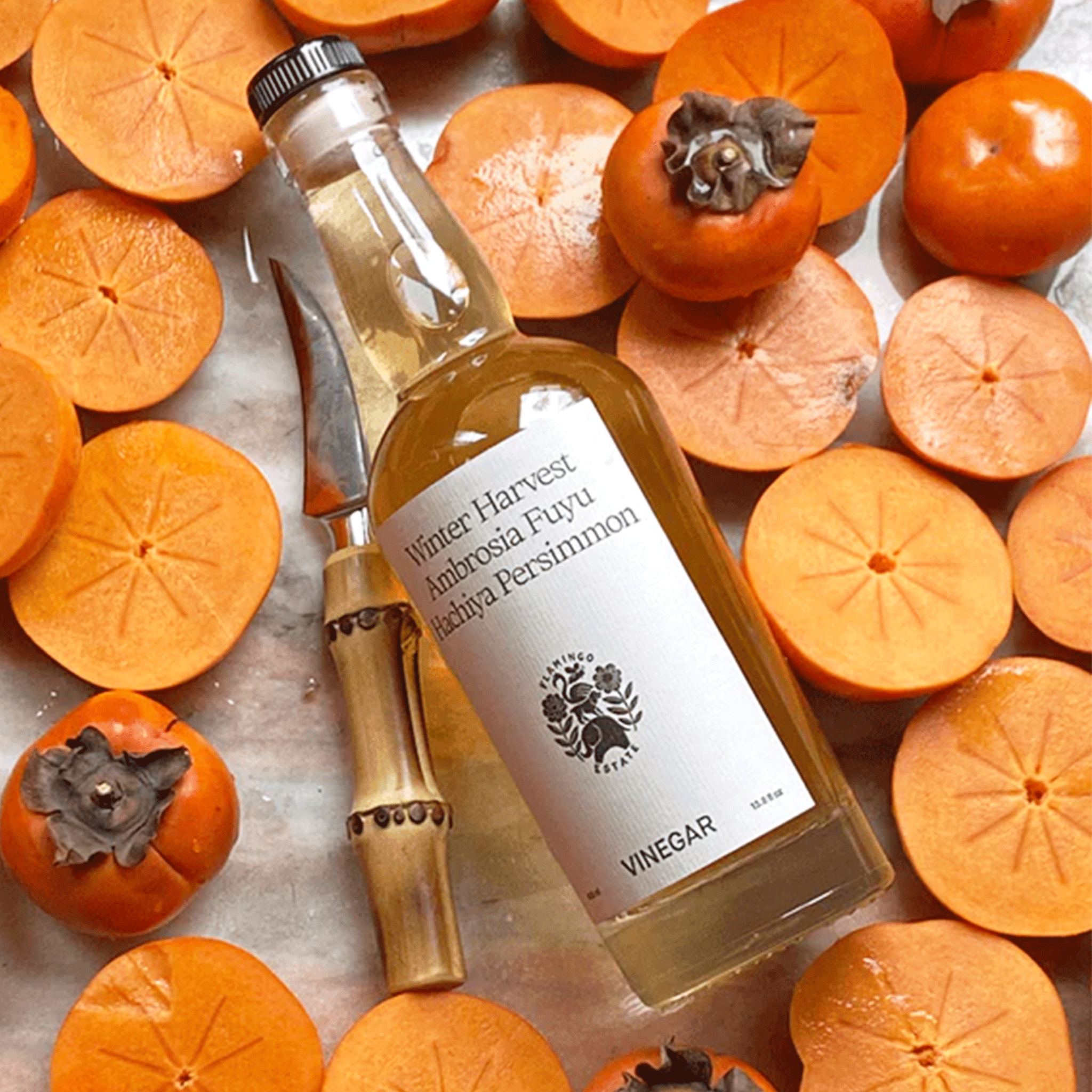 A clear bottle of persimmon vinegar with a white label on the front sitting on sliced persimmons. 