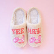 On a pink background is a pair of ivory slippers with pink western text that reads, "Yee" on one slipper and "Haw" on the other along with a graphic of pink cowgirl hats and cowgirl boots. 