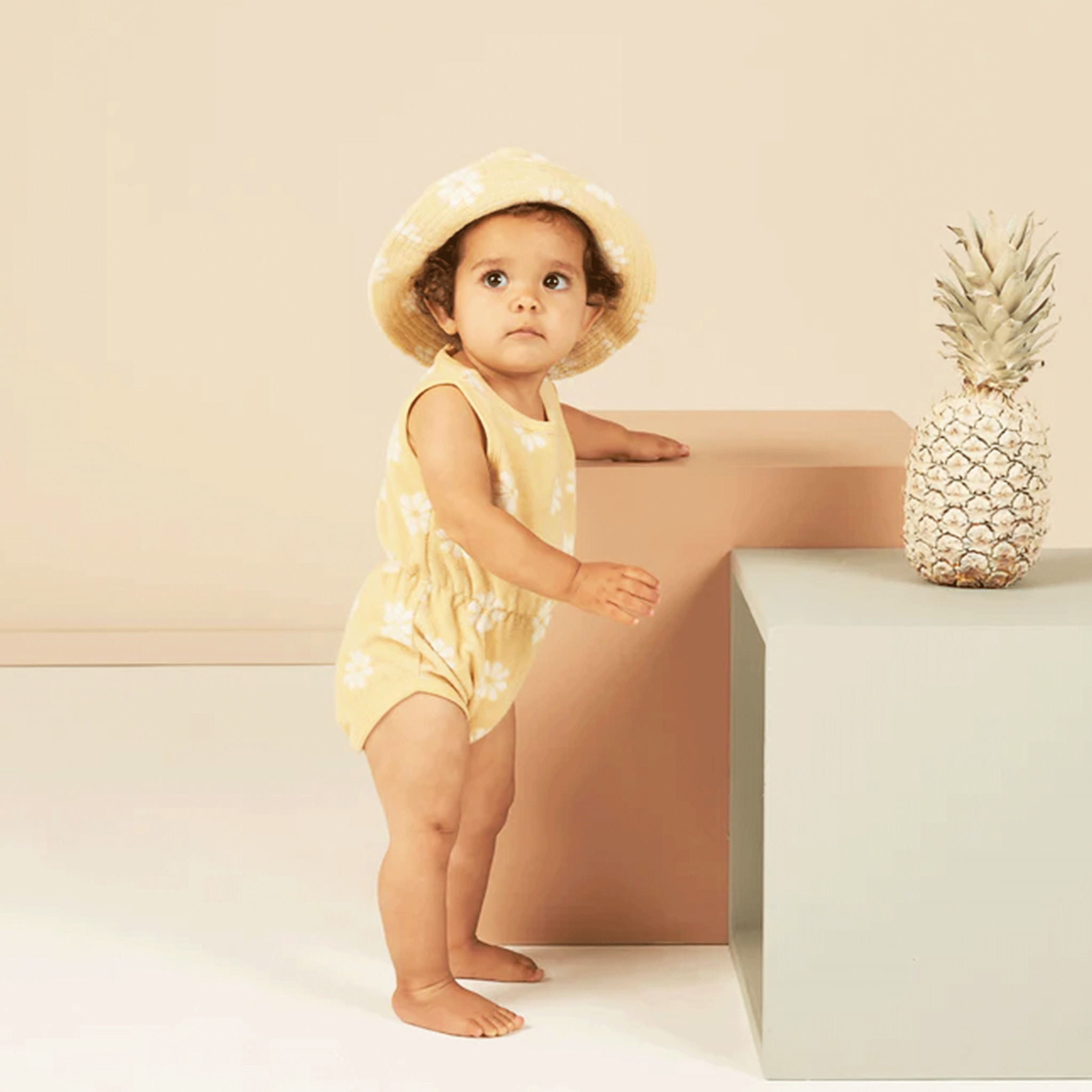 A terry cloth yellow playsuit for babies and toddlers with a white daisy print. Hat on model not included with purchase. 