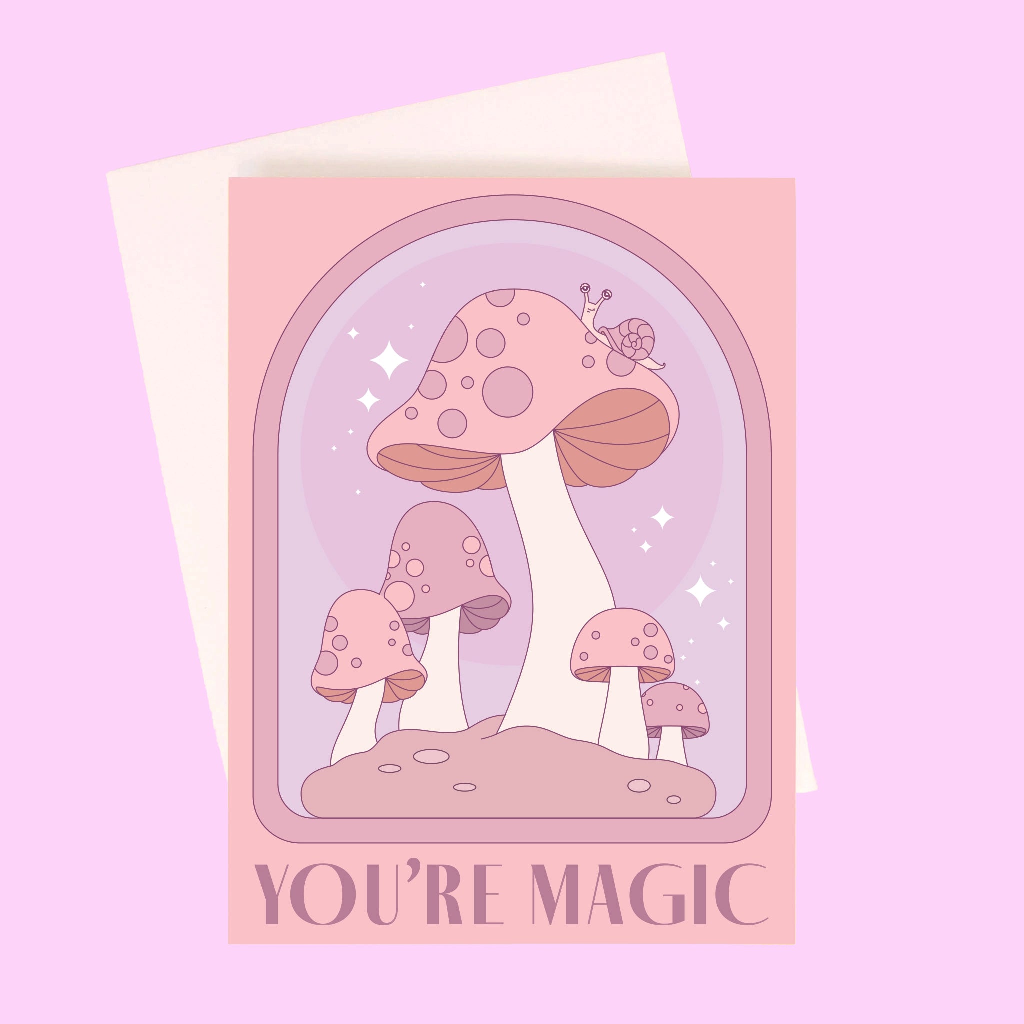 On a light purple background is a pink and purple card with an arch and mushroom design as well as text along the bottom that reads, "You're Magic". A white envelope is included with purchase, also shown here.