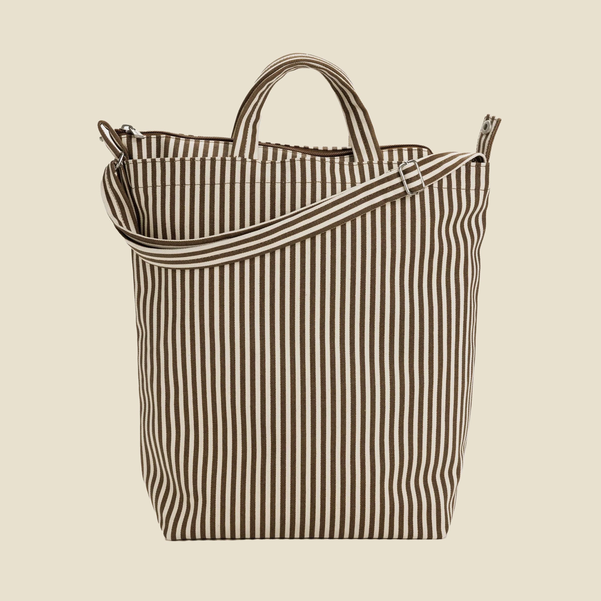 On a tan background is a brown and white stripe canvas tote bag with s hand bag and shoulder strap. 