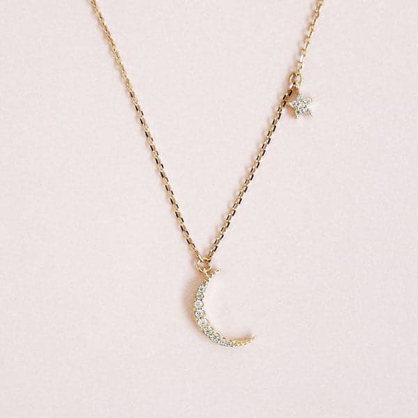 A dainty gold chain necklace with a crescent moon pendant filled with cubic zirconia stones and a small star pendant higher up on the chain also filled with cubic zirconia stones. 