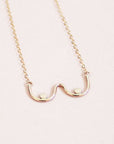 A gold chain necklace with a dainty pendant shaped like the outline of boobs.