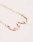 A gold chain necklace with a dainty pendant shaped like the outline of boobs.
