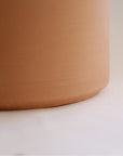 On a white background is a terracotta cylinder planter with a raw terracotta finish.