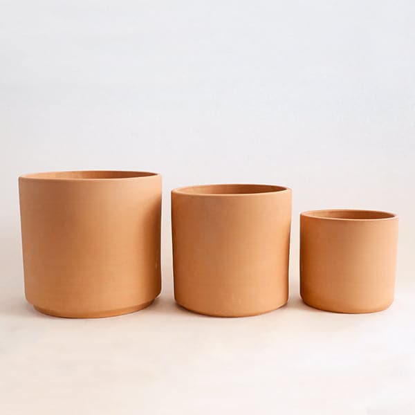 On a white background is a terracotta cylinder planter with a raw terracotta finish photographer here in all three sizes. 