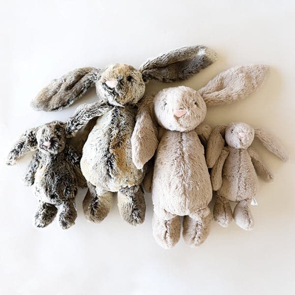 Four, two small and two large, soft stuffed animals in the shape of rabbits, with long floppy ears, arms and legs. Two small and large rabbits are a mottle grey and gold. The other two rabbits are a beige color.