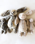 Four, two small and two large, soft stuffed animals in the shape of rabbits, with long floppy ears, arms and legs. Two small and large rabbits are a mottle grey and gold. The other two rabbits are a beige color.