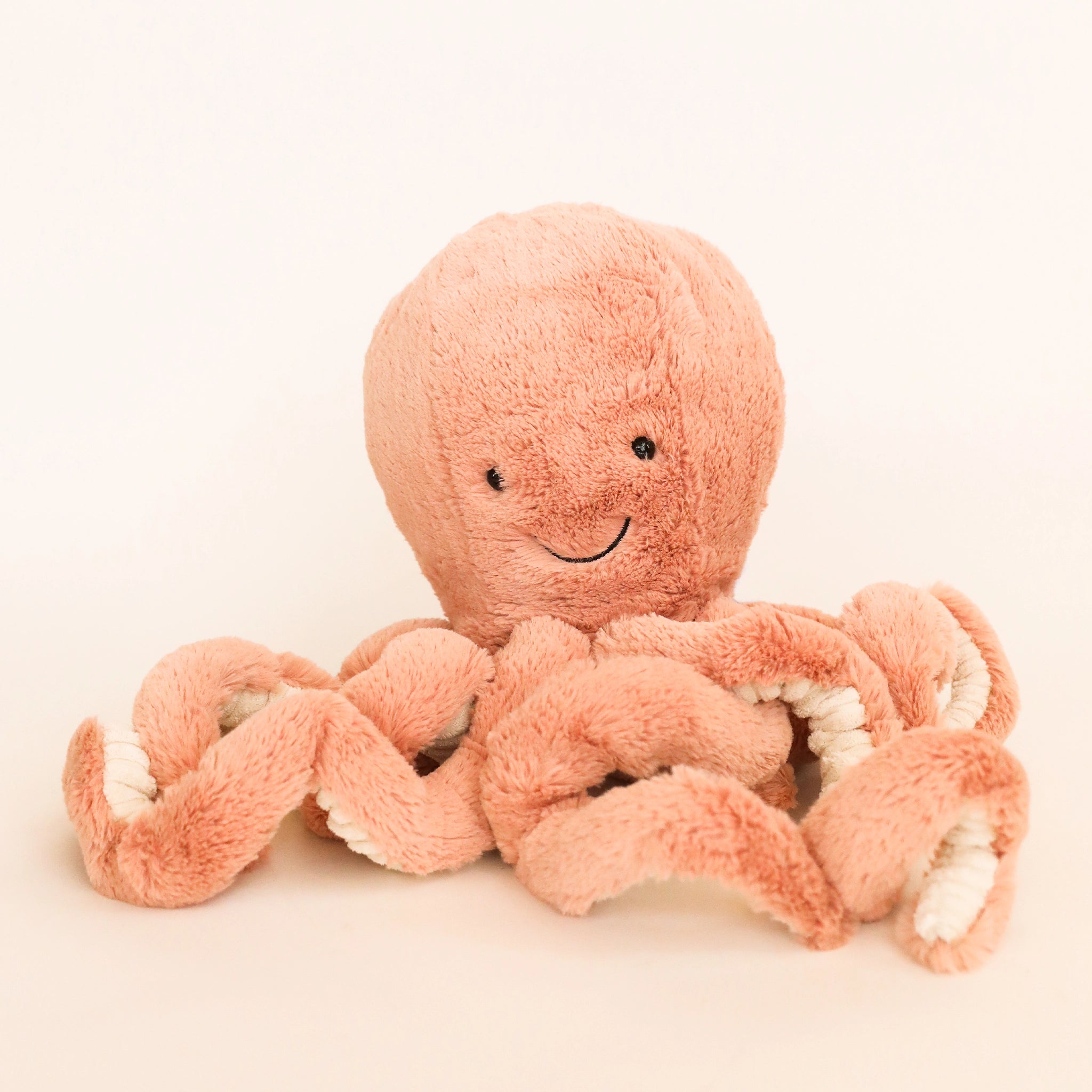 A pink octopus stuffed animal with a smiling face, photographed on a cream background. 