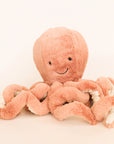 A pink octopus stuffed animal with a smiling face, photographed on a cream background.