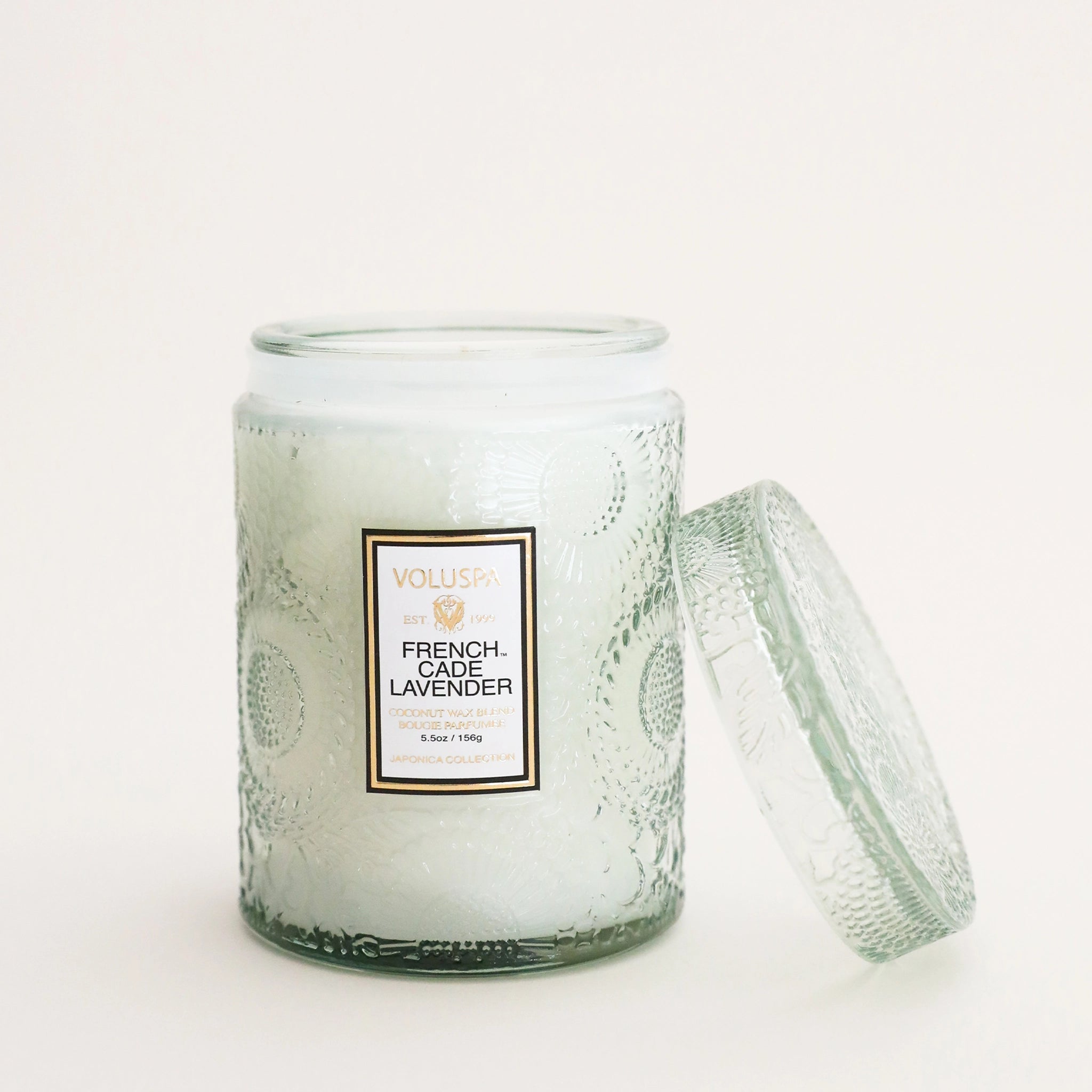A light green decorative glass jar candle with a white rectangular label that reads, &quot;French Cade Lavender&quot;.