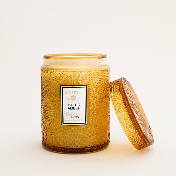 Flower textured gold translucent glass candle vessel with label, &quot;Voluspa. Baltic Amber.&quot;