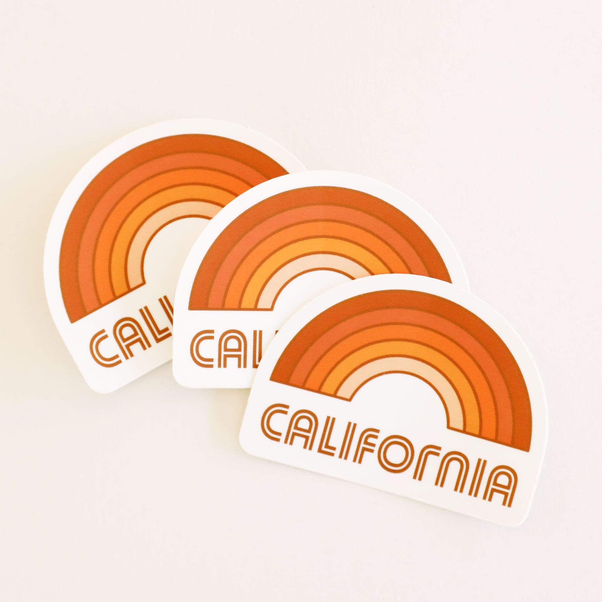 A rainbow sticker made up of different shades of orange and &quot;California&quot; written in orange letters on the bottom underneath the rainbow graphic.