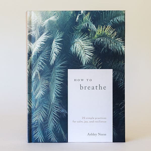 A hardcover book with green palms with a white rectangle in the bottom right hand corner of the front cover that reads, &quot;How to Breathe 25 simple practices for calm, joy and resilience, Ashley Neese&quot;.