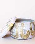 In front of a white background is a short, round tin. The tin is light pink with a gold floral pattern. There is a matching lid leaning against the left side of the tin.