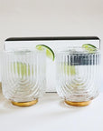 A clear glass tumbler with a gold base and an etched upside down arched design.