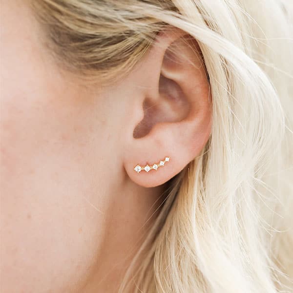 Single five-stone cascading crawlers feature white cubic zirconia placed in horizontal row and set in 18k gold-plated sterling silver. Earring is modeled on blonde woman and sits at the bottom of her earlobe. 